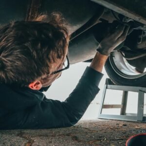 Mechanic skillfully repairing car undercarriage in outdoor setting with tools.